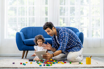 Modern Remote Communication Concept. Portrait of positive caucasian father making virtual video call with mother using tablet, while the little daughter was playing with colorful wooden blocks