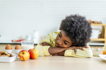 A little boy is sitting at the kitchen table leaning her face in her arms, concept for bullying,...