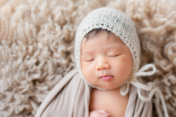 Fototapeta na wymiar Cute baby with beige wrap lying on the brown fur blanket.
