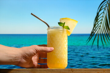 Beach bar, summer sea resort concept. Female hand holding a glass of melon smoothie on table bar. Drinking glass of melon lemonade cocktail.