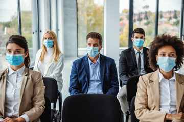Multiracial group of business people with face masks sitting on seminar during corona virus.