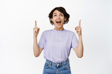 Image of amazed, super happy girl looking with fascinated, astonished face up, pointing fingers at logo, sale promo, showing advertisement, white background