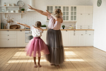 Little girl with mature grandmother wearing princess skirts showing funny dab gesture, standing in modern kitchen at home, adorable granddaughter with grandma dancing moving to favorite music © fizkes