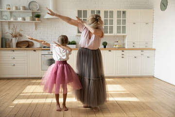 Little girl with mature grandmother wearing princess skirts showing funny dab gesture, standing in...