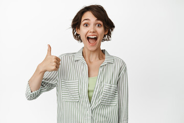Well done, awesome. Excited happy woman showing thumbs up, smiling and looking amazed, praise smth...