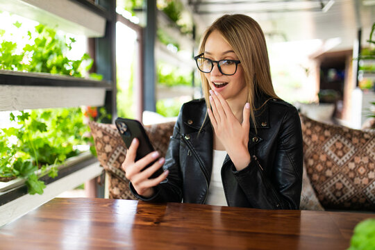 Image of a shocked young beautiful woman using mobile phone indoors in cafe.