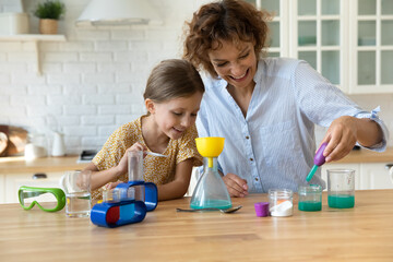 Happy mother with little girl playing scientists making funny experiments sitting at table with...