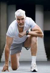 Portrait of a good looking gray haired senior man in white t-shirt in front of Olympic flag. Sport and health care concept