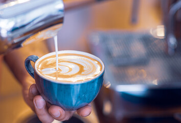 Barista preparing a latte in artistic mood, drawing a pattern to coffee.