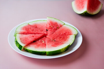 Pieces of watermelon on a round plate on a pink background. Top view, flat lay.
Ripe watermelon slices.
Vegetarian food.
Place for text