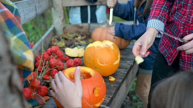 Family preparing halloween pumpkin. Hands carves a scary halloween pumpkin on a wooden bench in the garden. Making pumpkin decor for Halloween