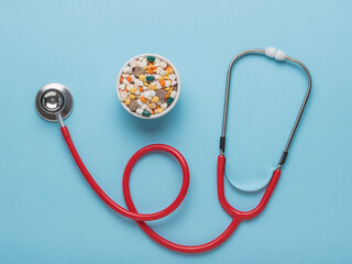 A red phonendoscope and a bowl of pills on a blue background. Flat lay.