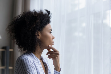 Fototapeta na wymiar Pensive millennial African American woman look in window distance thinking pondering of life problems. Thoughtful unhappy young biracial female make plan consider. Dilemma, lockdown concept.