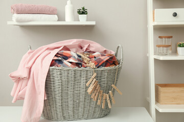 Wicker basket with dirty laundry and clothespins on table indoors
