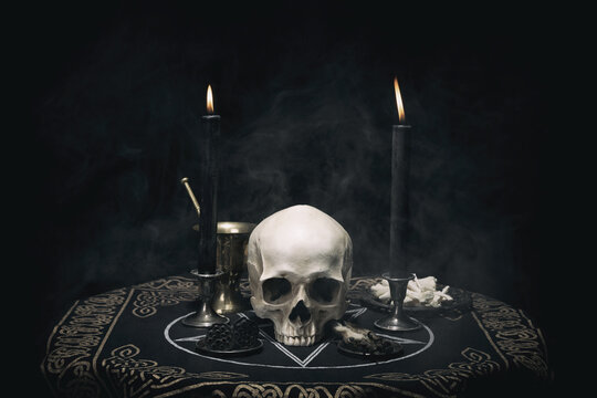 Witchcraft composition with burning candles, human skull, bones, herbs and pentagram symbol. Halloween and occult concept, black magic ritual. 