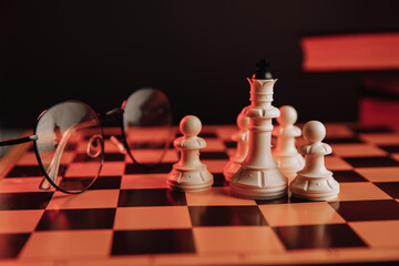 White chess pieces on the chessboard with books and glasses close-up