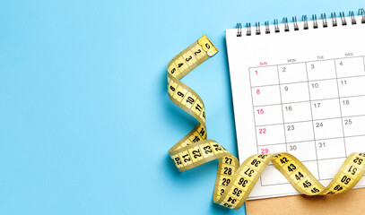 Calendar and yellow measuring tape. Weight loss diet or workout concept. Blue background. Template Copy space for text