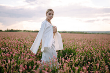 Fototapeta na wymiar Beauty romantic girl Outdoors at sunset. Young woman in stylish clothes posing in the blooming field. Nature, vacation, relax and lifestyle. Fashion concept.