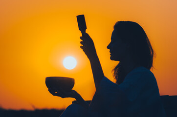 Cinematic silhouette of woman playing a Tibetan bowl at gorgeous orange sunset with sun disk....