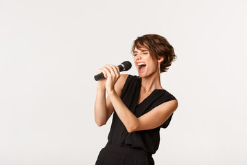 Carefree attractive girl singing in microphone, performing, have fun at karaoke, standing over...