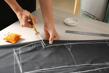 Seamstress cutting fabric following chalked sewing pattern at table in workshop, closeup