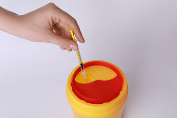Woman throwing used syringe into sharps container on white background, closeup