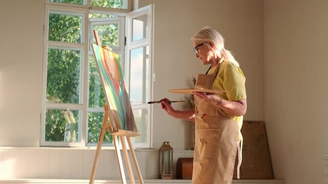Senior Artist, Art Workshop, Sun Rays, Painting Woman. Senior woman artist paints a picture on canvas