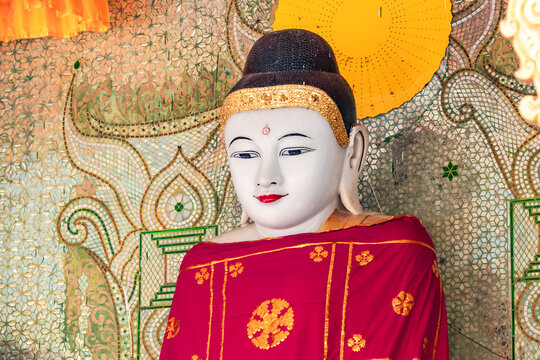 Eine reich verzierte Buddha-Statue mit rotem Gewand in einem Tempel der Shwedagon Pagode im burmesischen Yangon