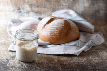 Sourdough for baking bread in a jar and bread on an old table. Homebaked bread. Concept: healthy eating. Selective focus.