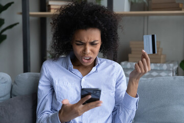 Unhappy young African American woman confused with bankruptcy or debt shopping online on cellphone...