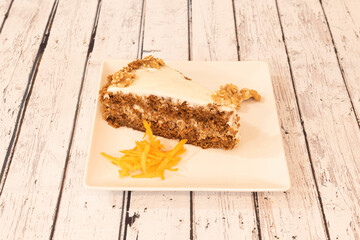 Portion of carrot cake with delicious sponge cake with pieces of dried fruits, walnuts on top and white frosting