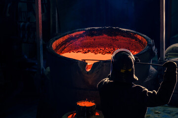 rear view of a worker in a metal workshop near a vat of molten metal