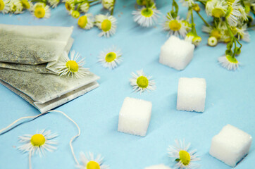 Obraz na płótnie Canvas two tea bags, sugar cubes, chamomile wildflowers on a blue background, chamomile tea, top view