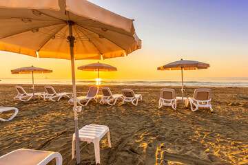 tranqiul sunrise an a beautiful beach with umbrellas on thr foreground , golden sand and sun rays and calm sea on the background
