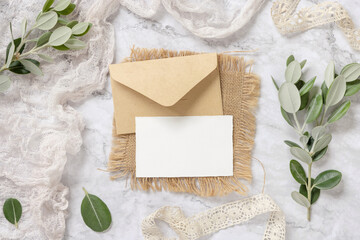 Blank card with envelope laying on a marble table decorated with eucalyptus branches