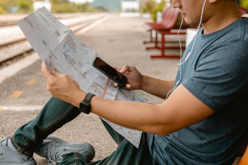 Traveler is using smartphone while planning vacation with map at railway station. Man is planning vacation and looking the map.