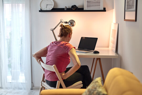 Woman working on a laptop at home and having problems with hips, back and stomack ache.