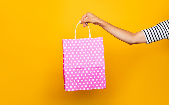 Close up photo of female hand with colorful shopping bag in hands isolated on yellow background