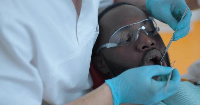 Close-up an African American male patient who is having a mouth cavity inspection by the male dentist.
