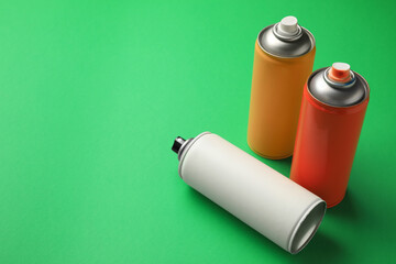 Cans of different spray paints on green background, space for text. Graffiti supplies