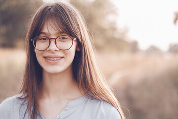Portrait of a smiling brown-haired teenager girl with glasses and dental braces.