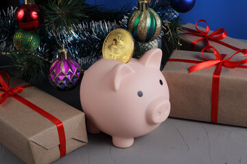 piggy bank pig with gold bitcoin under a christmas tree decorated with christmas balls and tinsel, close-up