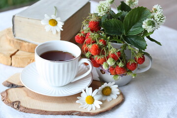 Still life of a cup of tea, strawberries and daisies. There is a place for text. Romantic summer morning. Selective focus.