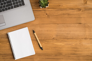 Top view photo of laptop flowerpot pen and workbook on isolated wooden table background with empty space