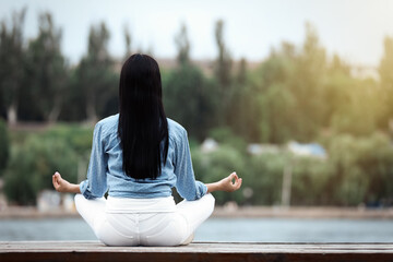 Young woman meditating near river, back view. Space for text