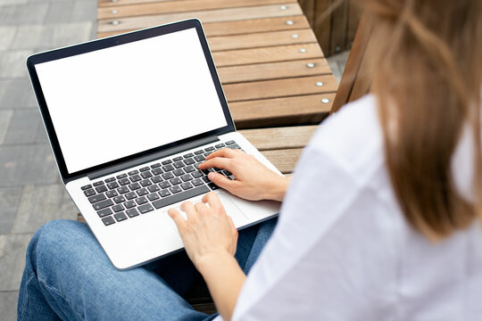 Mockup image blank white screen laptop. woman hands texting using laptop relax on bench in the middle of the street. background empty space for advertise text. 