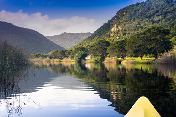 Scenic river canoe trip with tranquil reflections of mountains and trees on river edge near Knysna...