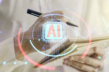 Double exposure of creative artificial Intelligence abbreviation with man hand writing in notepad on background. Future technology and AI concept