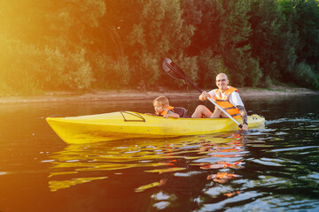 Cheerful father and his toddler son kayaking on a big wide river.