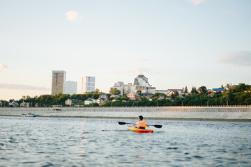 Longshot of a man kayaking on a big wide river next to a concrete riverbank